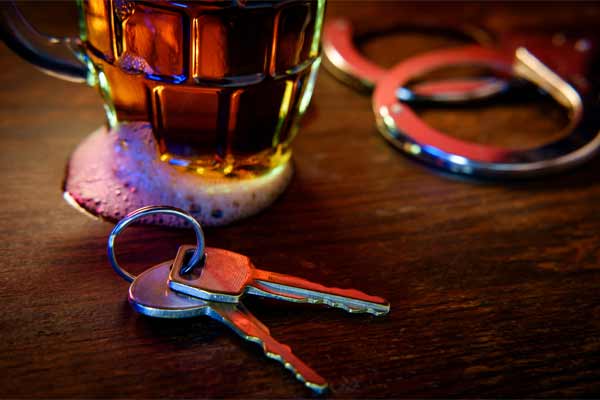 A beer, car keys, and handcuffs on a bar.